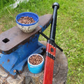 Blue anvil on a stump with two bowls of coffee beans and a red and black sheathed sword outdoors.