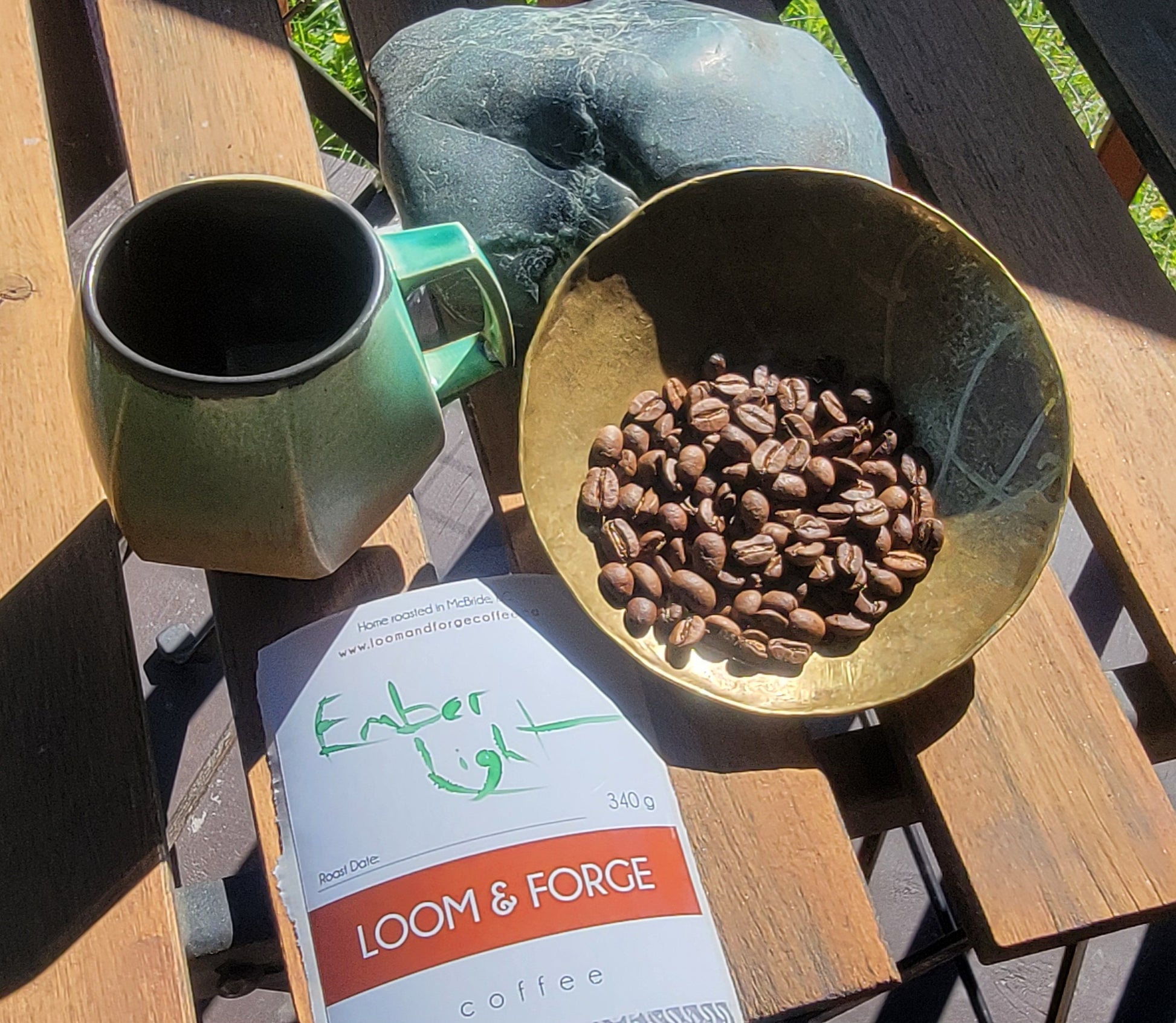 Green mug, gold bowl with coffee beans, and 'Ember Light' coffee package on a wooden surface.